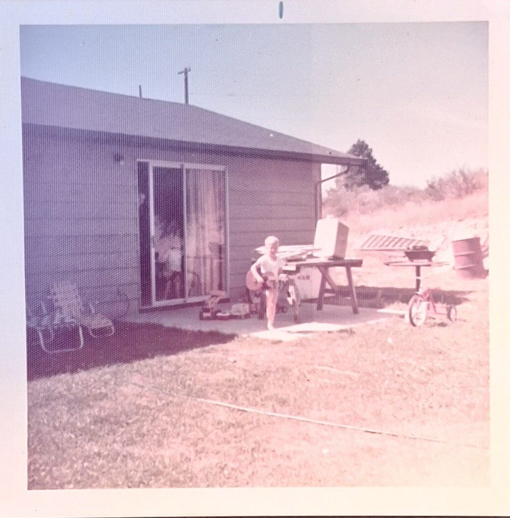 RJH at six years old, holding a guitar outside a house